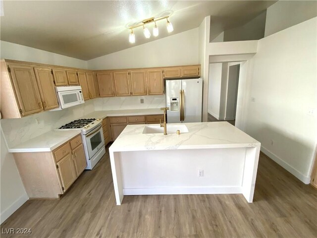 kitchen with white appliances, a kitchen island with sink, sink, hardwood / wood-style floors, and lofted ceiling