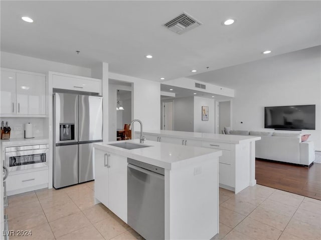 kitchen with sink, light tile patterned floors, an island with sink, white cabinets, and appliances with stainless steel finishes