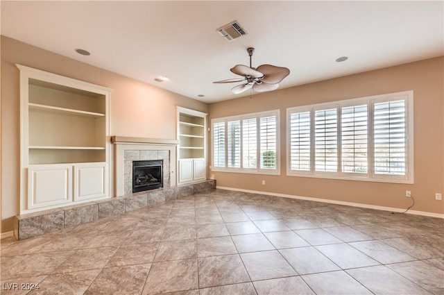 unfurnished living room featuring ceiling fan, a healthy amount of sunlight, built in features, and a tiled fireplace