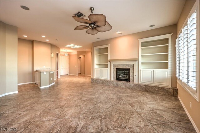 unfurnished living room featuring a wealth of natural light, built in features, ceiling fan, and a premium fireplace