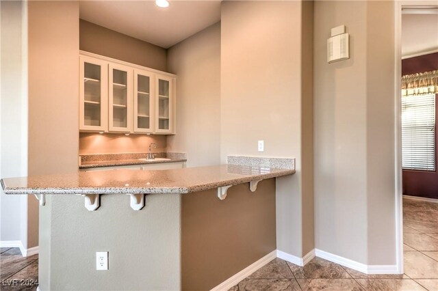 kitchen featuring a kitchen bar, light tile patterned floors, kitchen peninsula, and sink