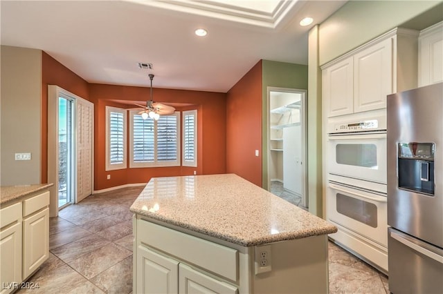 kitchen with white double oven, stainless steel fridge, decorative light fixtures, a kitchen island, and light stone counters