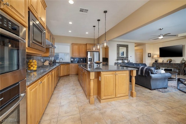 kitchen with a kitchen island, appliances with stainless steel finishes, sink, dark stone countertops, and hanging light fixtures