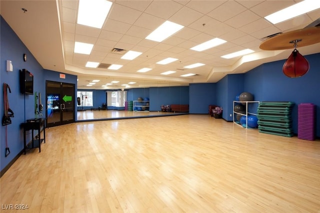 workout area with a tray ceiling, light hardwood / wood-style flooring, and a drop ceiling