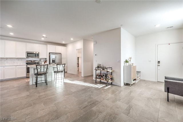 kitchen featuring decorative backsplash, appliances with stainless steel finishes, a kitchen breakfast bar, a kitchen island, and white cabinetry