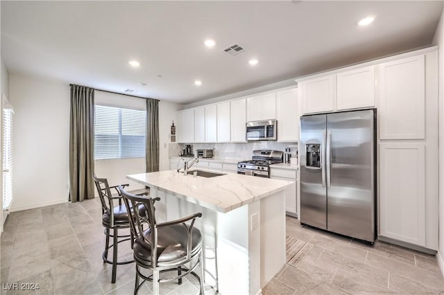 kitchen featuring white cabinetry, sink, light stone counters, an island with sink, and appliances with stainless steel finishes