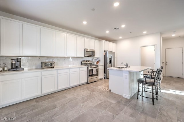 kitchen featuring a kitchen bar, appliances with stainless steel finishes, a kitchen island with sink, sink, and white cabinets