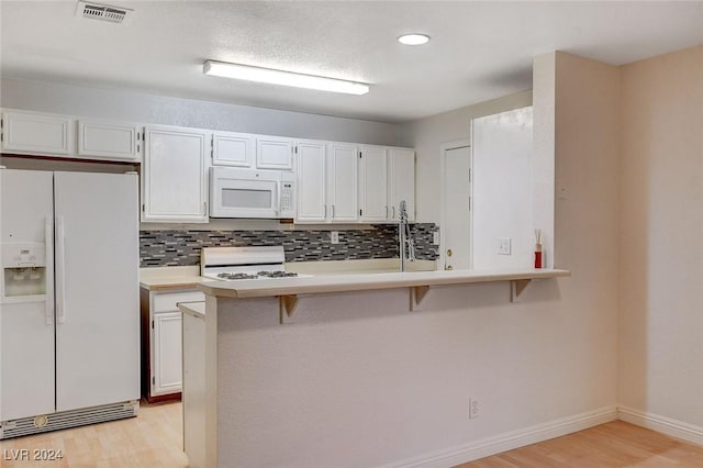 kitchen with white cabinetry, a breakfast bar, white appliances, and kitchen peninsula