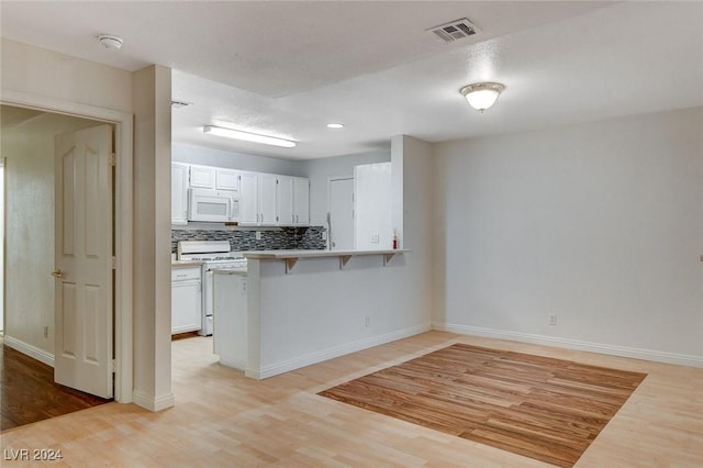 kitchen featuring a breakfast bar area, white cabinets, white appliances, kitchen peninsula, and light wood-type flooring