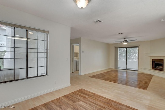 unfurnished living room featuring ceiling fan, washer / dryer, light hardwood / wood-style floors, and a tile fireplace