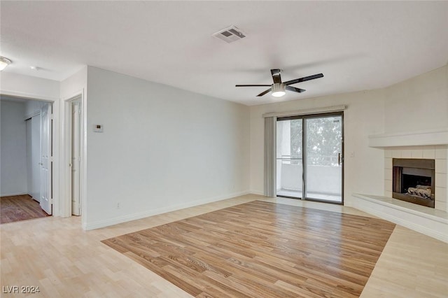 unfurnished living room with ceiling fan, a tiled fireplace, and light hardwood / wood-style floors