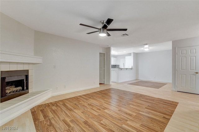 unfurnished living room featuring a tiled fireplace, ceiling fan, and light hardwood / wood-style flooring