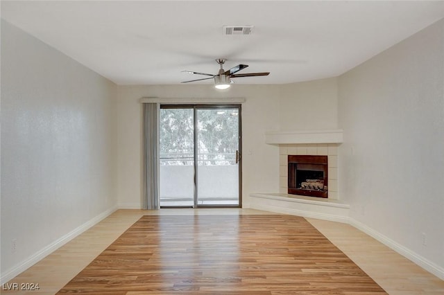 unfurnished living room with a tile fireplace, ceiling fan, and light wood-type flooring