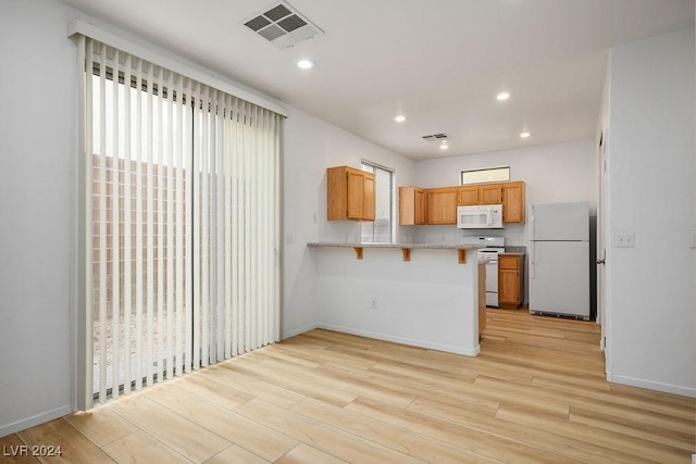 kitchen featuring a kitchen bar, white appliances, kitchen peninsula, and light hardwood / wood-style flooring