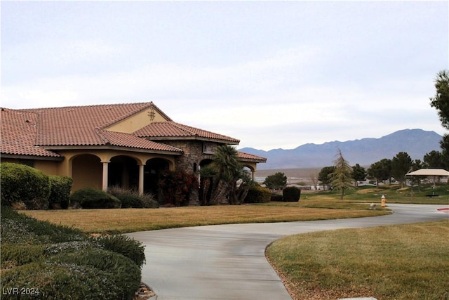 exterior space with a mountain view, a tiled roof, concrete driveway, stucco siding, and a front lawn