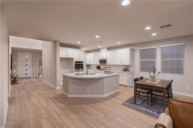 kitchen with white cabinets, light wood-type flooring, stainless steel appliances, and an island with sink