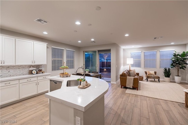 kitchen with white cabinetry, sink, light hardwood / wood-style flooring, backsplash, and a center island with sink