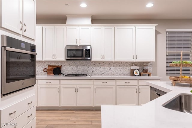 kitchen with sink, light hardwood / wood-style floors, decorative backsplash, white cabinets, and appliances with stainless steel finishes