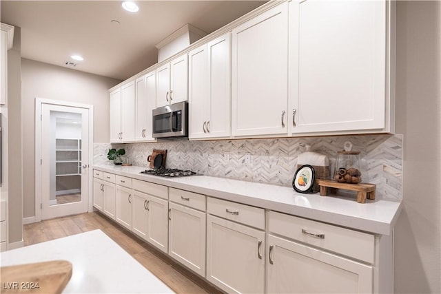 kitchen featuring white cabinetry, stainless steel appliances, light stone counters, backsplash, and light hardwood / wood-style floors