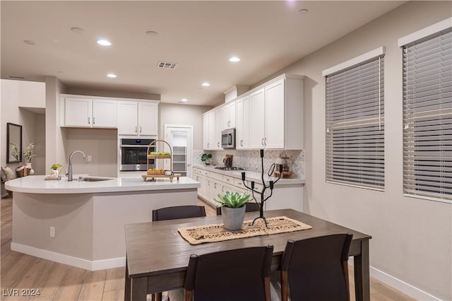 kitchen with sink, an island with sink, tasteful backsplash, white cabinetry, and stainless steel appliances