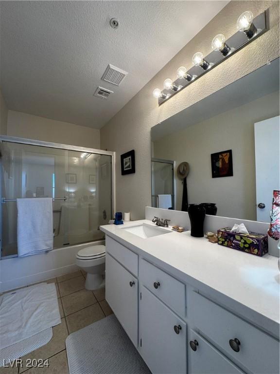 full bathroom with vanity, a textured ceiling, enclosed tub / shower combo, tile patterned flooring, and toilet