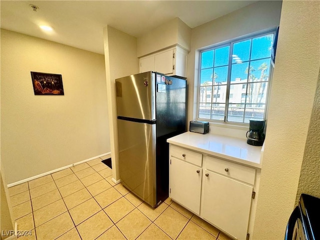 kitchen with light tile patterned floors, white cabinetry, stainless steel refrigerator, and range