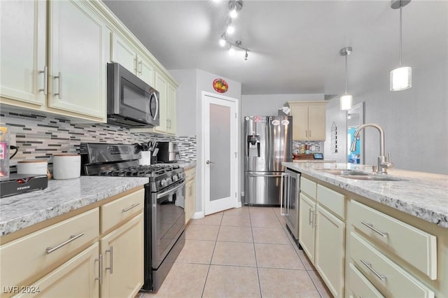 kitchen with appliances with stainless steel finishes, light stone counters, sink, light tile patterned floors, and pendant lighting