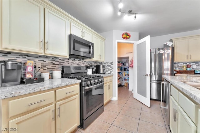 kitchen featuring backsplash, cream cabinets, appliances with stainless steel finishes, light tile patterned flooring, and light stone counters