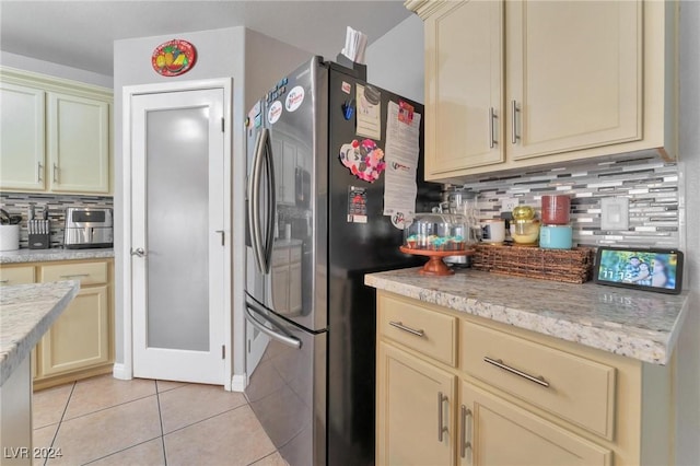 kitchen featuring decorative backsplash, cream cabinets, stainless steel refrigerator, and light tile patterned flooring