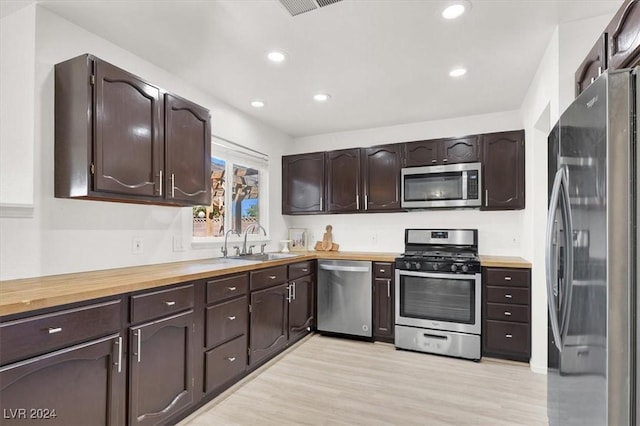 kitchen with wood counters, sink, appliances with stainless steel finishes, dark brown cabinets, and light hardwood / wood-style floors