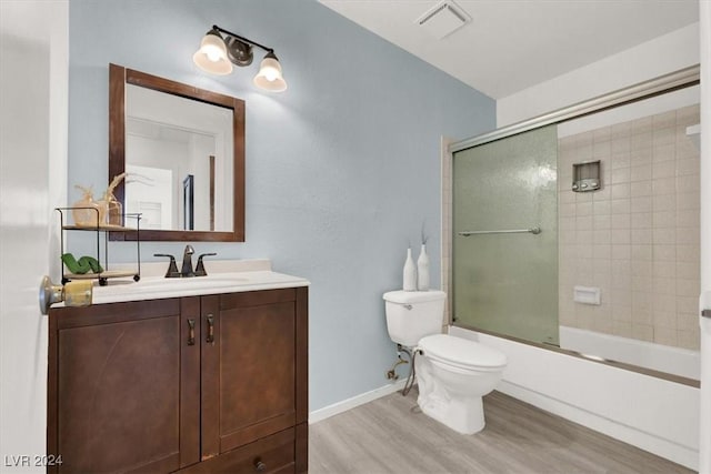 full bathroom featuring hardwood / wood-style flooring, vanity, toilet, and shower / bath combination with glass door