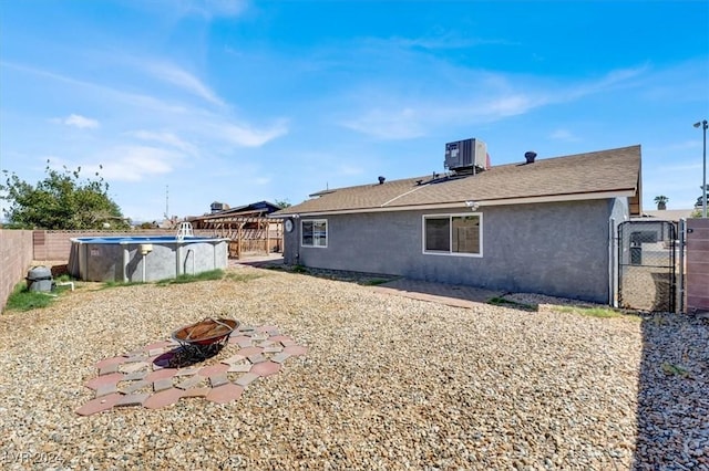 rear view of house featuring central AC, a fenced in pool, and a fire pit