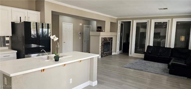 kitchen featuring sink, black fridge, a fireplace, white cabinets, and light wood-type flooring