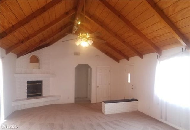 unfurnished living room with wooden ceiling, carpet, ceiling fan, a brick fireplace, and lofted ceiling with beams