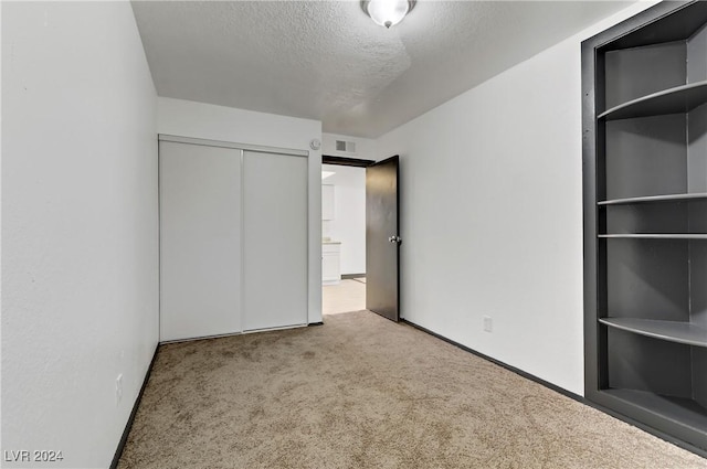 unfurnished bedroom featuring light carpet, a textured ceiling, and a closet