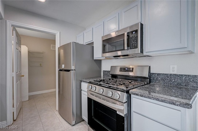 kitchen featuring light tile patterned floors, dark stone countertops, white cabinetry, and appliances with stainless steel finishes