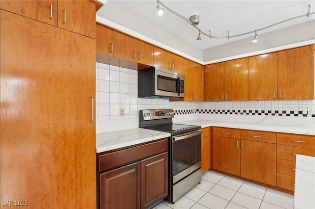 kitchen with stainless steel appliances, light tile patterned flooring, light stone counters, and decorative backsplash