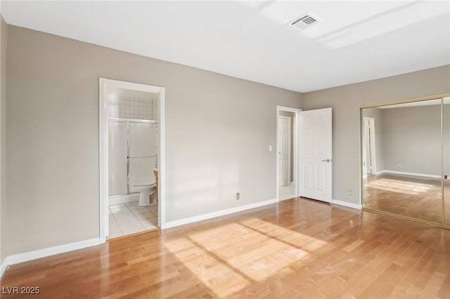 unfurnished bedroom with ensuite bath, wood-type flooring, and a closet