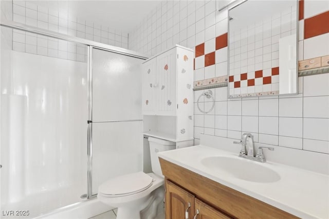 bathroom with vanity, toilet, a shower with door, and tile walls