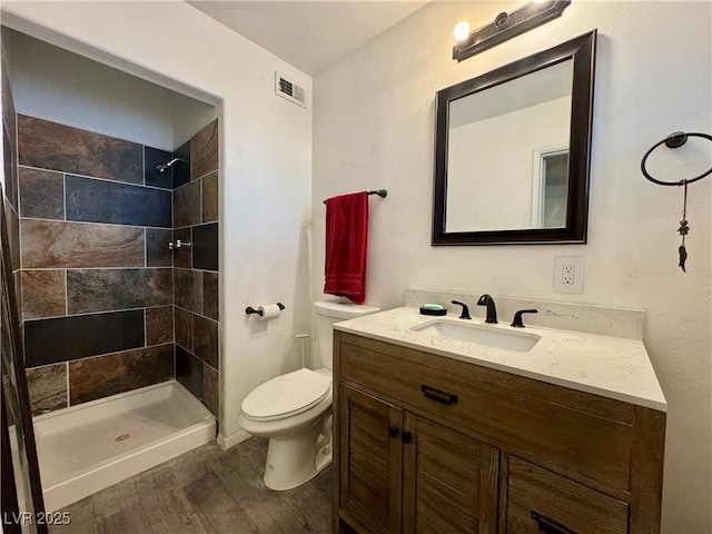 bathroom featuring visible vents, toilet, a tile shower, vanity, and wood finished floors