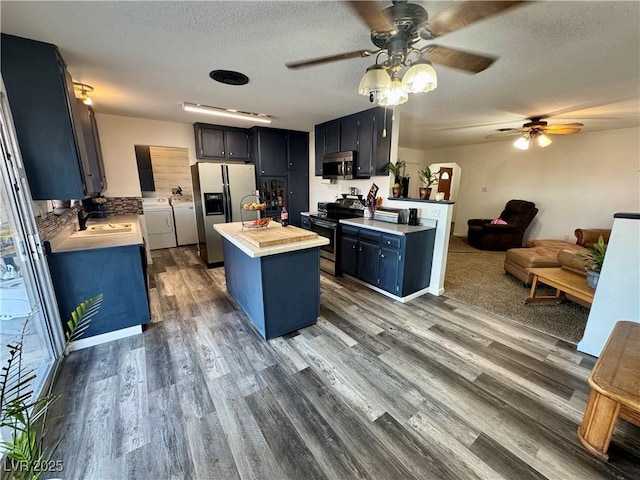 kitchen with wood finished floors, light countertops, appliances with stainless steel finishes, a center island, and washing machine and clothes dryer