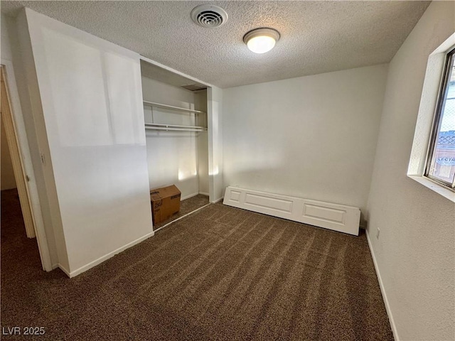 unfurnished bedroom with dark colored carpet, a closet, visible vents, a textured ceiling, and baseboards