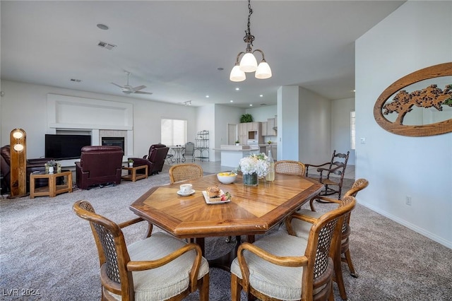 dining space with a tiled fireplace, light carpet, and ceiling fan with notable chandelier