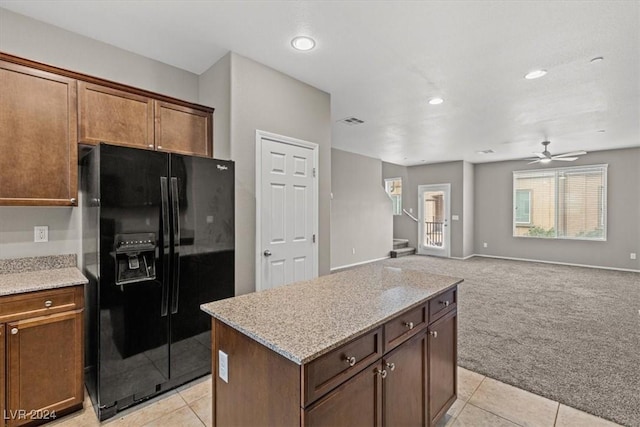 kitchen featuring light carpet, light stone countertops, black refrigerator with ice dispenser, ceiling fan, and a center island