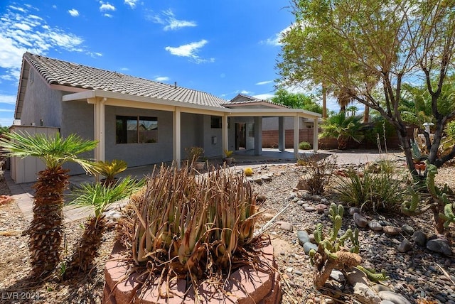 back of house with stucco siding, fence, and a tile roof