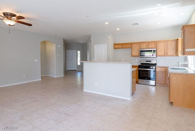 kitchen featuring arched walkways, a sink, stainless steel appliances, open floor plan, and tasteful backsplash