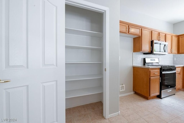 kitchen featuring brown cabinets, backsplash, stainless steel appliances, light countertops, and baseboards