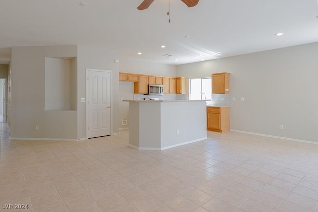 kitchen featuring stainless steel microwave, backsplash, ceiling fan, open floor plan, and light countertops