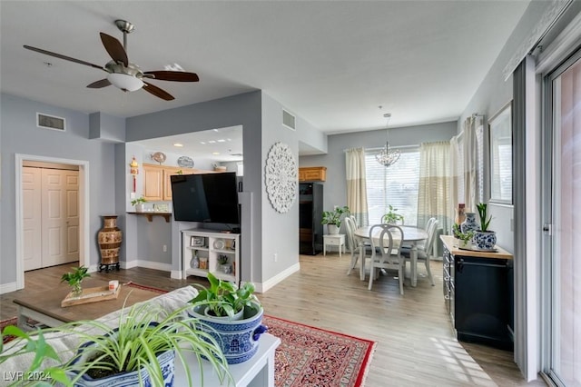 living room featuring ceiling fan with notable chandelier and light wood-type flooring