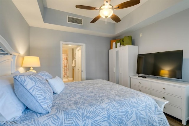 bedroom featuring a raised ceiling, ensuite bath, and ceiling fan